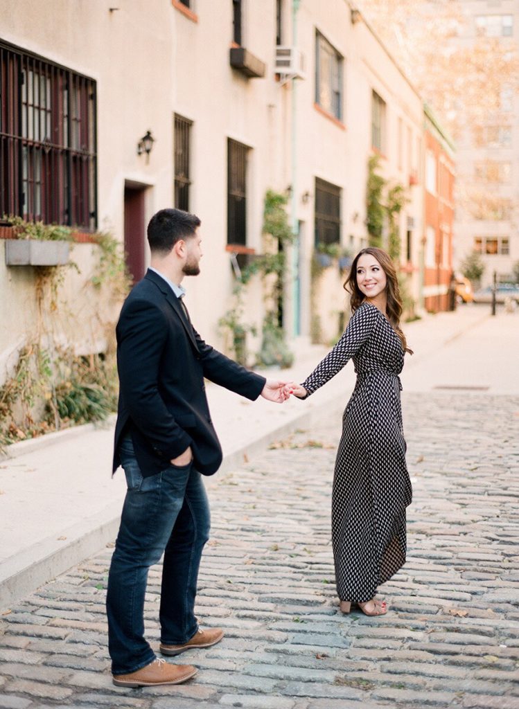 A woman leading her fiance down Washington Mews during engagement photos in NYC with You Look Lovely Photography