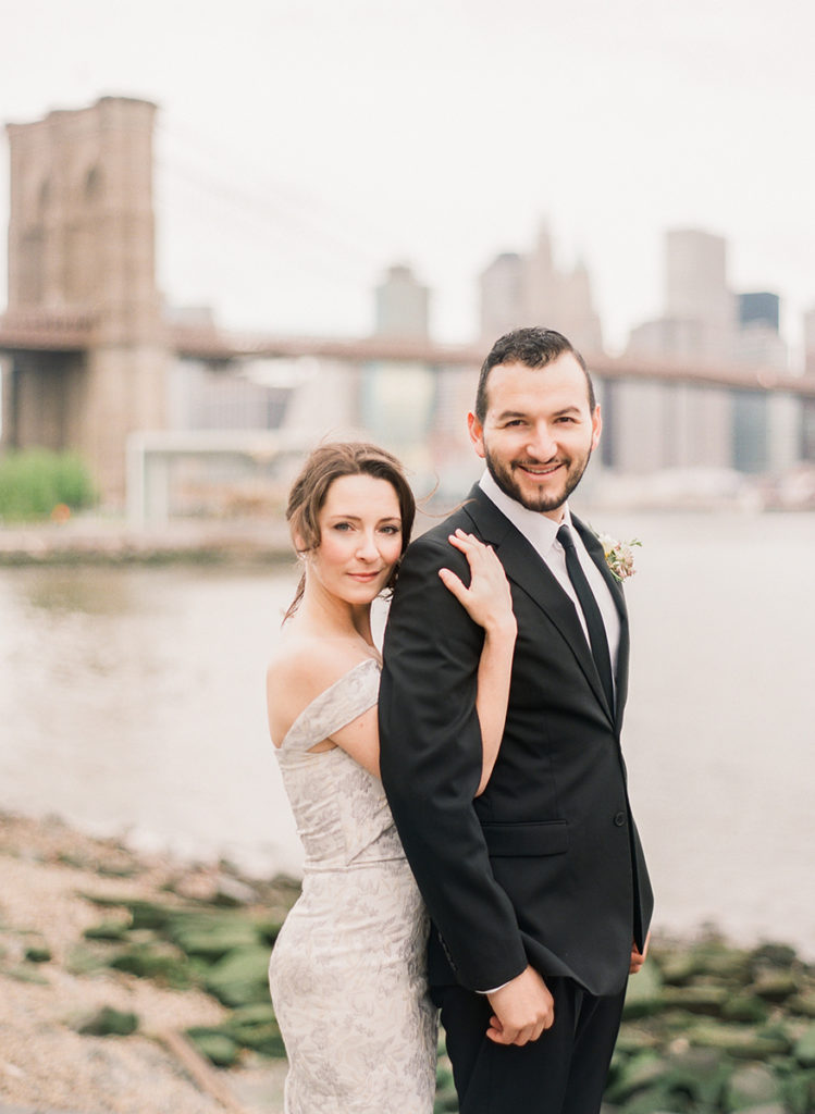 Romantic couple at Brooklyn Bridge Park with the bridge and city behind them during NYC engagement photos by You Look Lovely Photography