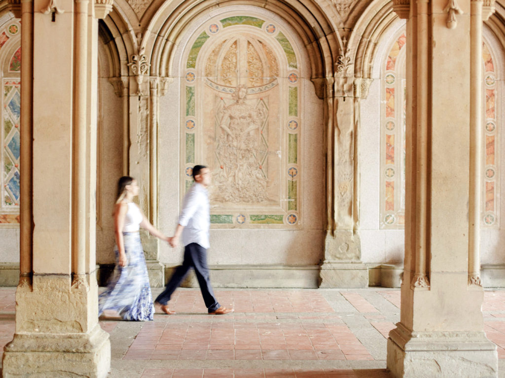 A motion blur photo of a couple during engagement photos in NYC, swiftly walking hand and hand through the Bethesda Fountain Acrade in Central Park photographed by You Look Lovely Photography