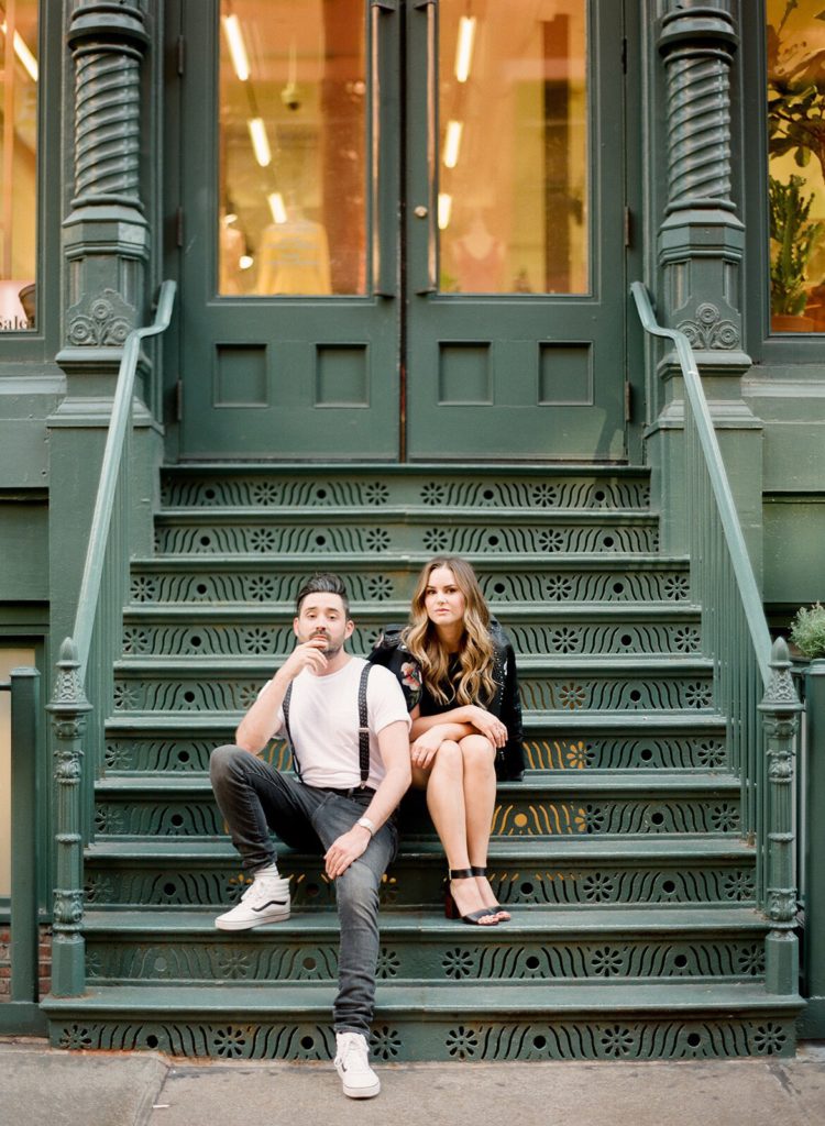 A young stylish couple sitting on a green staircase in SoHo during NYC engagement photos