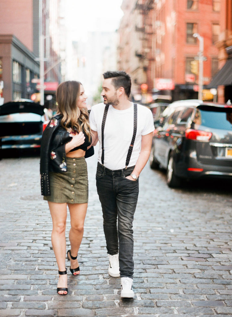 A young couple in love holding hands and walking along the cobblestone streets in SoHo NYC during an editorial engagement session with You Look Lovely Photography