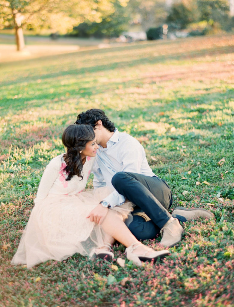 A couple sitting close together in the grass during engagement photos in NYC at Riverside Park