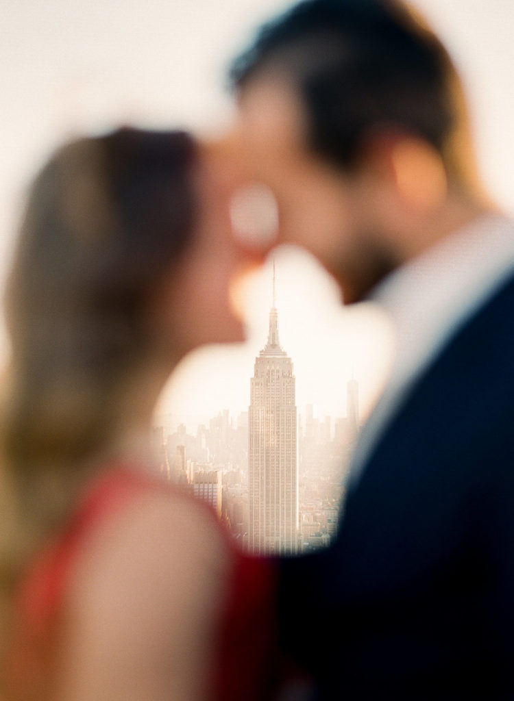 A romantic image showing the Empire State Building framed by a blurred out couple with their heads touching photographed by You Look Lovely Photography during engagement photos in NYC