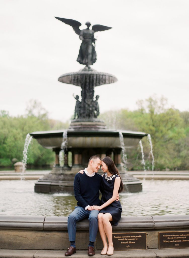 A young couple embracing on the edge of Bethesda Fountain during Central Park engagement photos in NYC photographed by You Look Lovely Photography