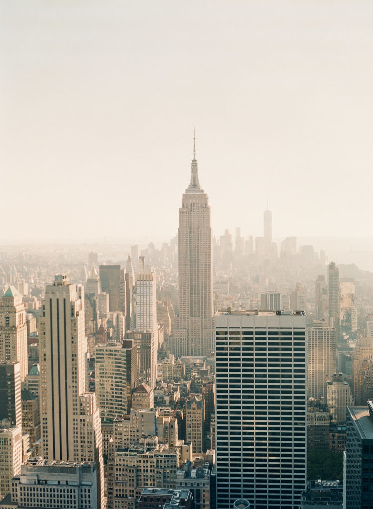 An image by You Look Lovely Photography of NYC from the Top of the Rock looking south at the Empire State Building and Midtown Manhattan with the Freedom Tower in the distance during romantic NYC engagement photos