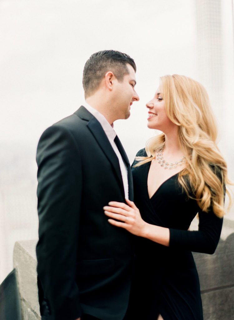 A couple staring lovingly into each other's eyes at Top of the Rock during an NYC engagement photoshoot by You Look Lovely Photography