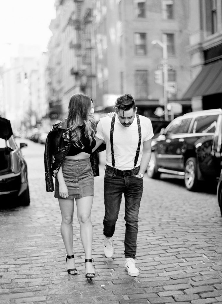 A stylish couple captured in black and white walking on the cobblestone streets of SoHo NYC during their editorial engagement session with You Look Lovely Photography