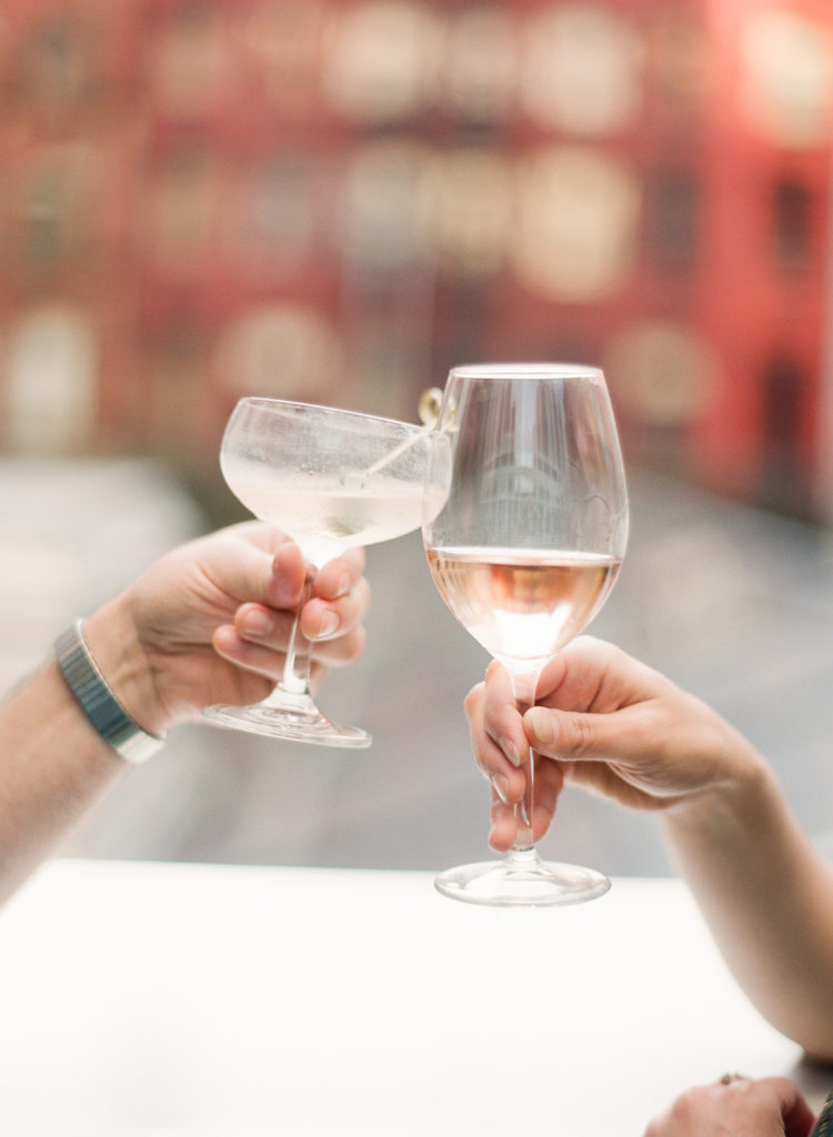 An artistic photo of a couples hands toasting featuring a reflection of historic SoHo buildings in their glasses during their editorial style engagement photos with You Look Lovely 