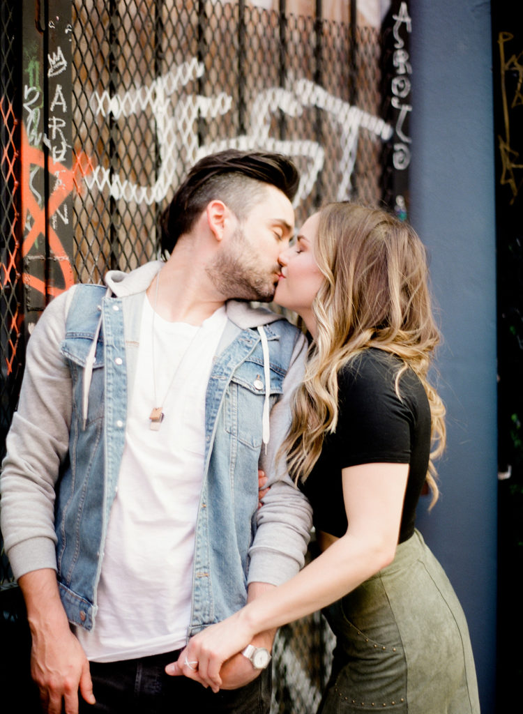 A stylish couple kiss in front of graffiti art for their SoHo street engagement photos with You Look Lovely Photography