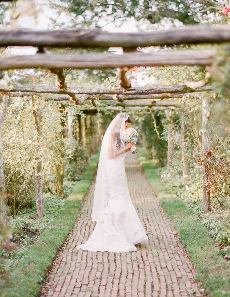 A veiled bride smelling her bouquet in a garden photographed by You Look Lovely Photography