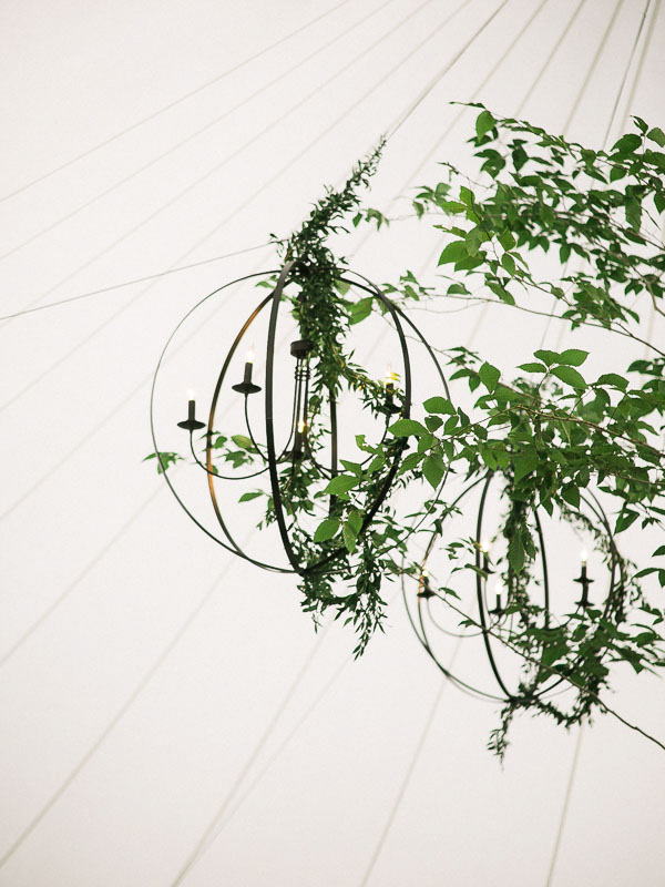 Greenery hanging from round chandeliers inside of a sail cloth wedding tent photographed by You Look Lovely Photography