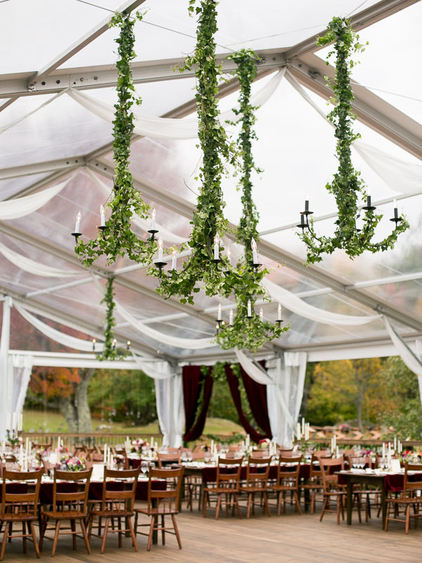 Vine-wrapped chandeliers and long wedding reception tables in a clear tent at a private Vermont estate in the fall photographed by You Look Lovely Photography