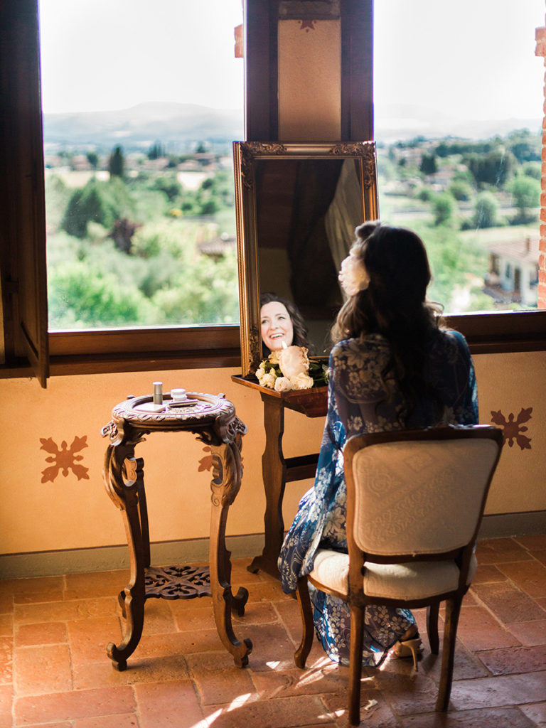 A destination wedding bride looking out of the windows in her room that overlook the rolling hills of Tuscany as she gets ready photographed by You Look Lovely Photography