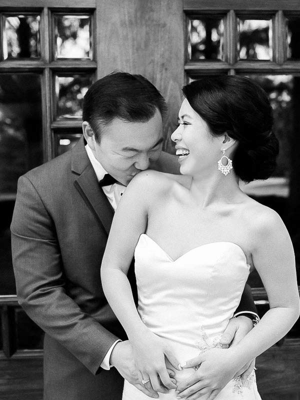 A black and white image of a groom kissing a laughing brides shoulder photographed by You Look Lovely Photography